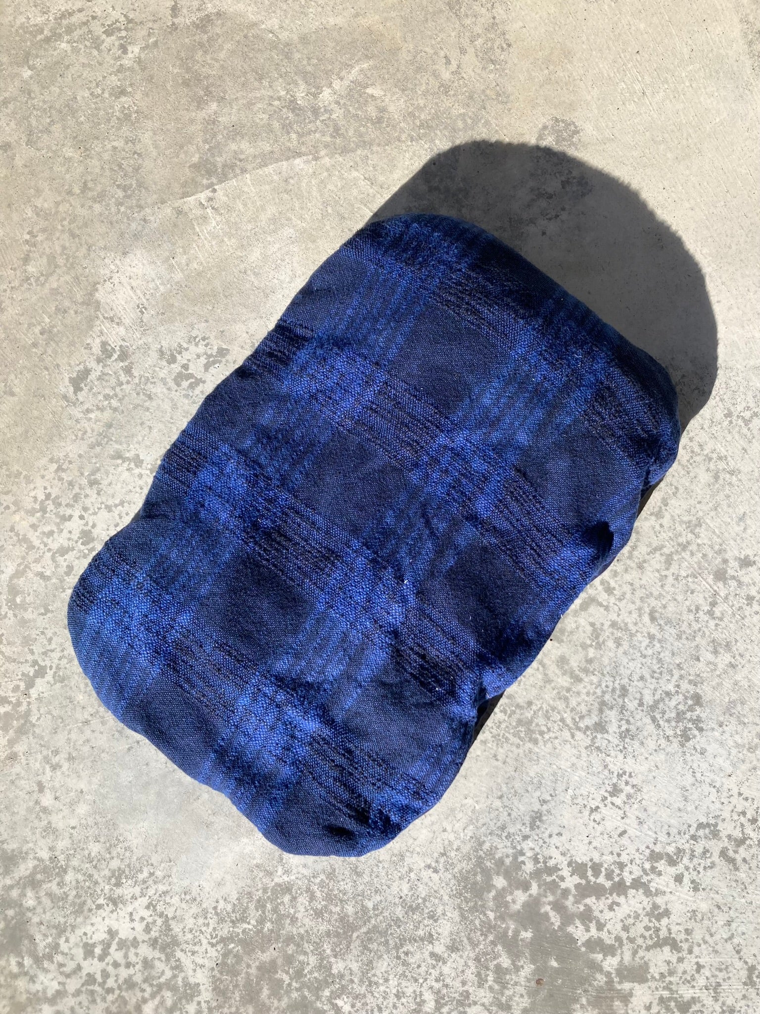 The woven blue pet pillow placed at an angle on a concrete background.