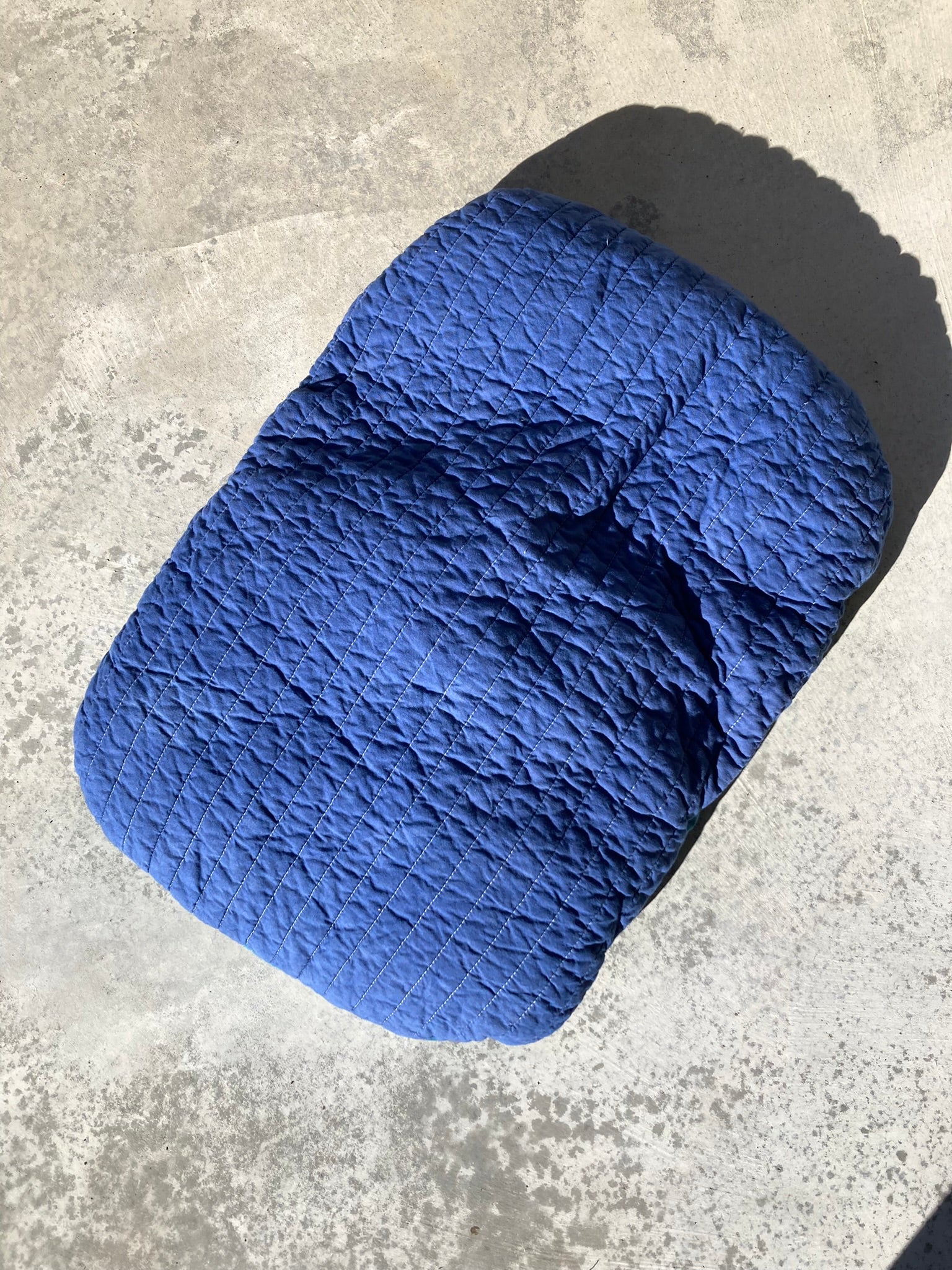 The bright blue pet pillow placed at an angle on a concrete background.