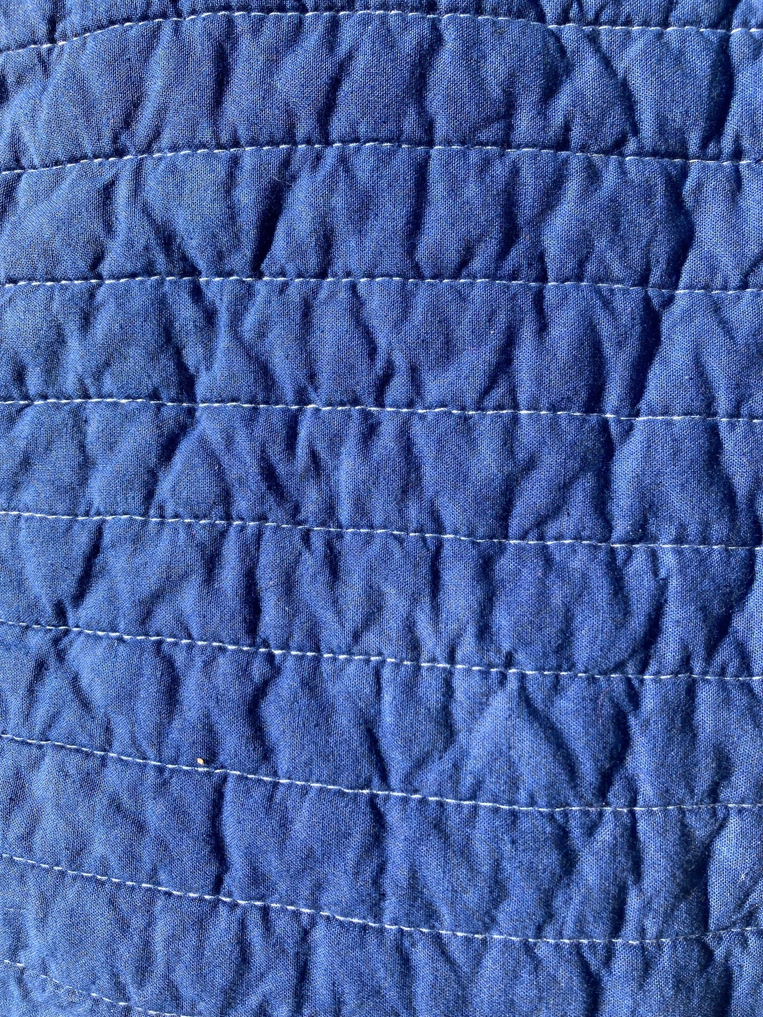 Close-up of the bright blue pet pillow top, showing the slight variation in blue due to the hand-dye process. Also shows the straight line quilting in white thread going horizontally.