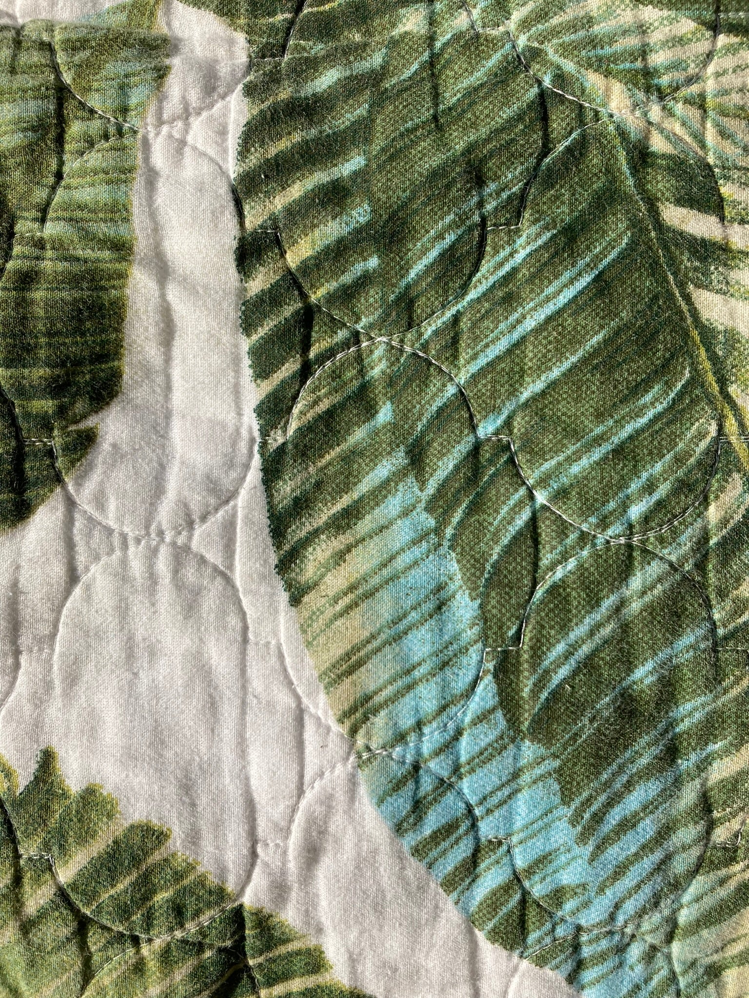 Close-up of the tropical pet pillow top. The fabric has a cream/beige background and palm leaves in forest green, light green and a faded turquoise. 