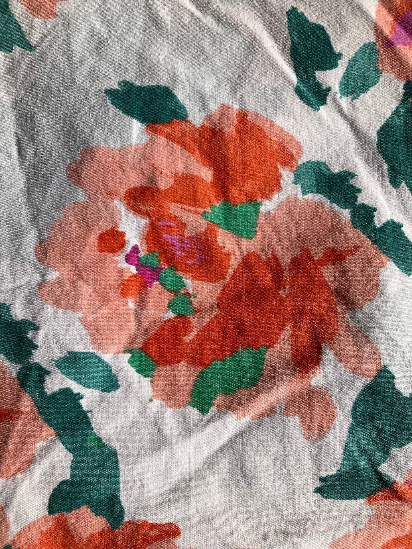 Close-up of the backing for the emerald pet pillow.  The fabric has a white backing with a painterly floral pattern in reds, oranges, fuschia with emerald leaves.