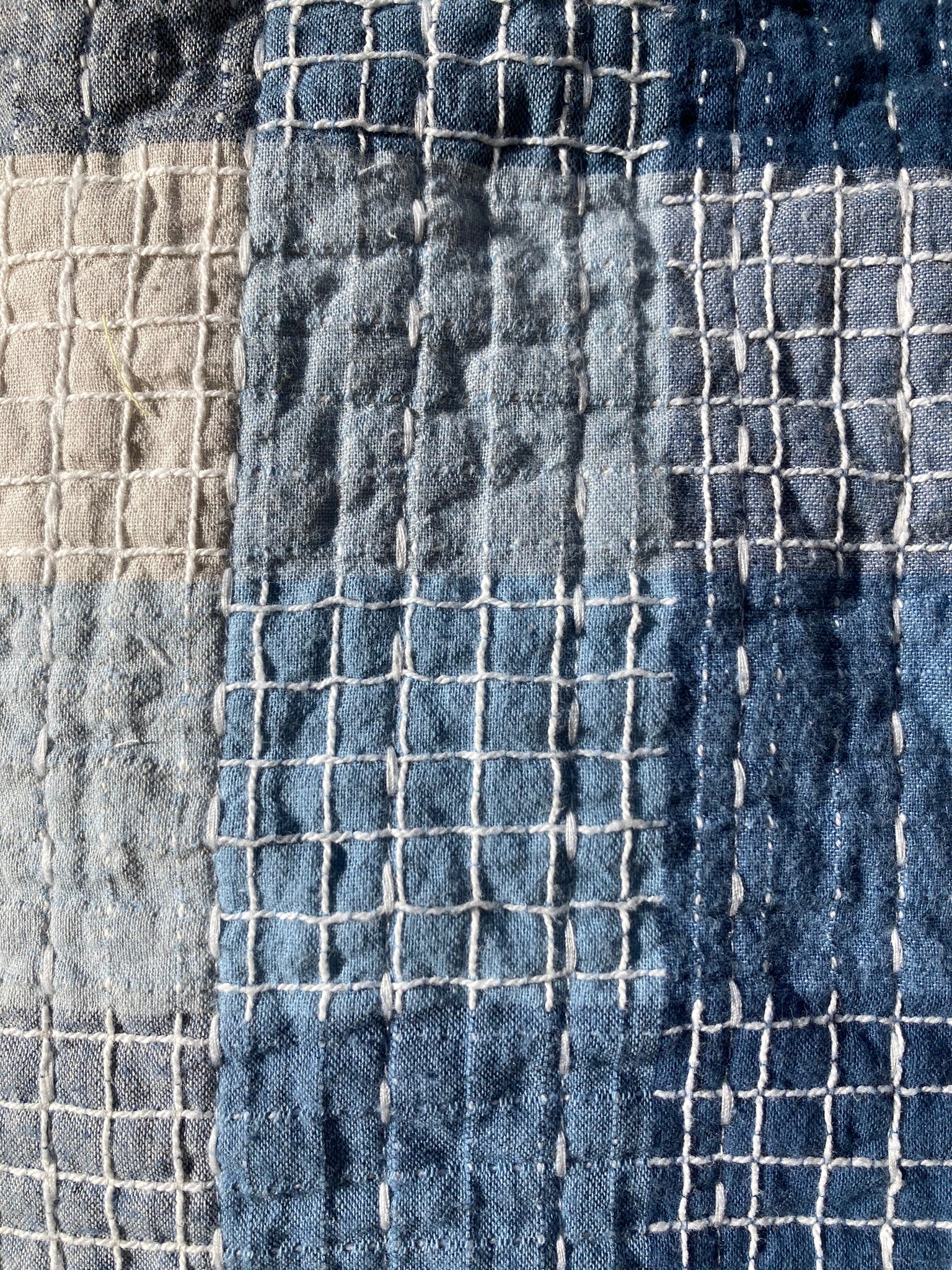 Close-up of the patchwork pet pillow top shows the squares of different blue and grey as well as the varied quilting patterns in thick white thread.